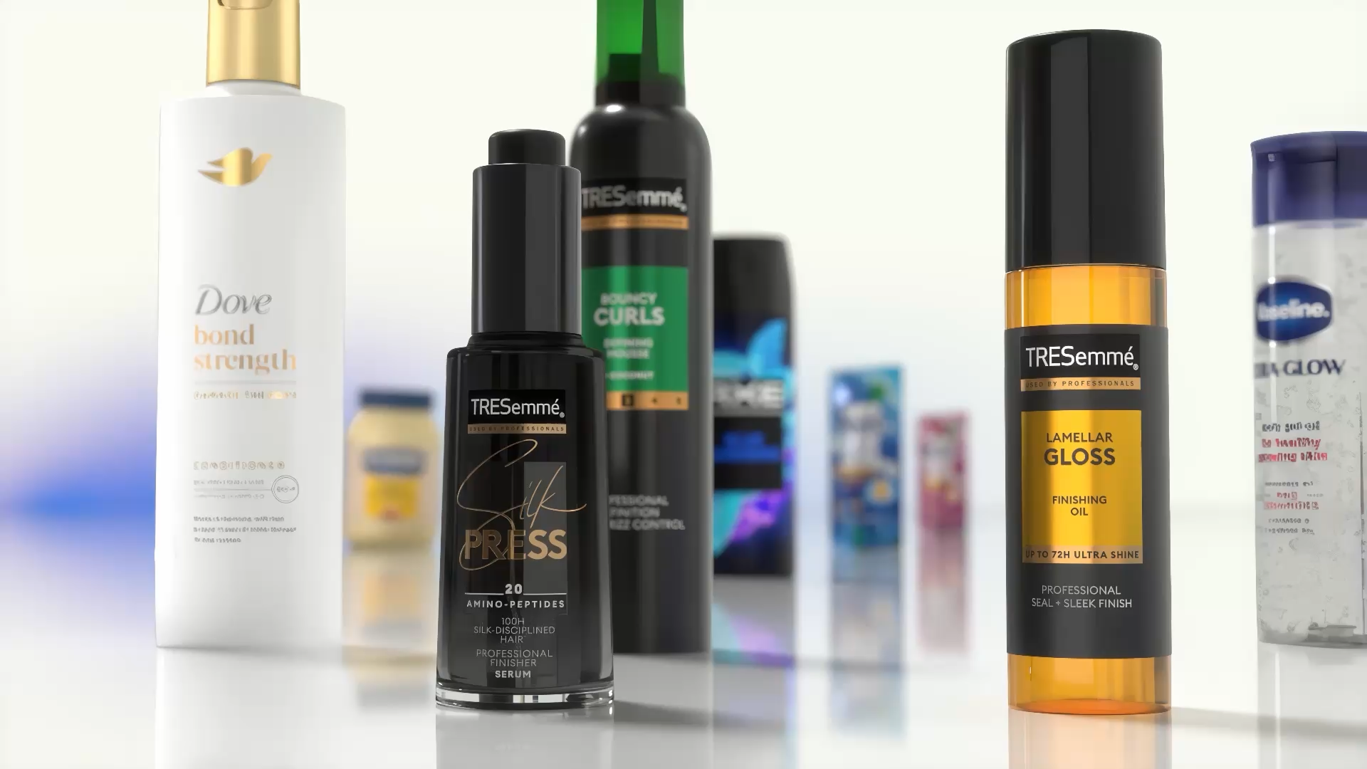 Close-up van diverse haar- en lichaamsverzorgingsproducten tentoongesteld op een reflecterend oppervlak. Zichtbaar zijn onder andere Dove Bond Strength conditioner, TRESemmé Silk Press serum, TRESemmé Lamellar Gloss finishing oil en andere Unilever-producten op de achtergrond.