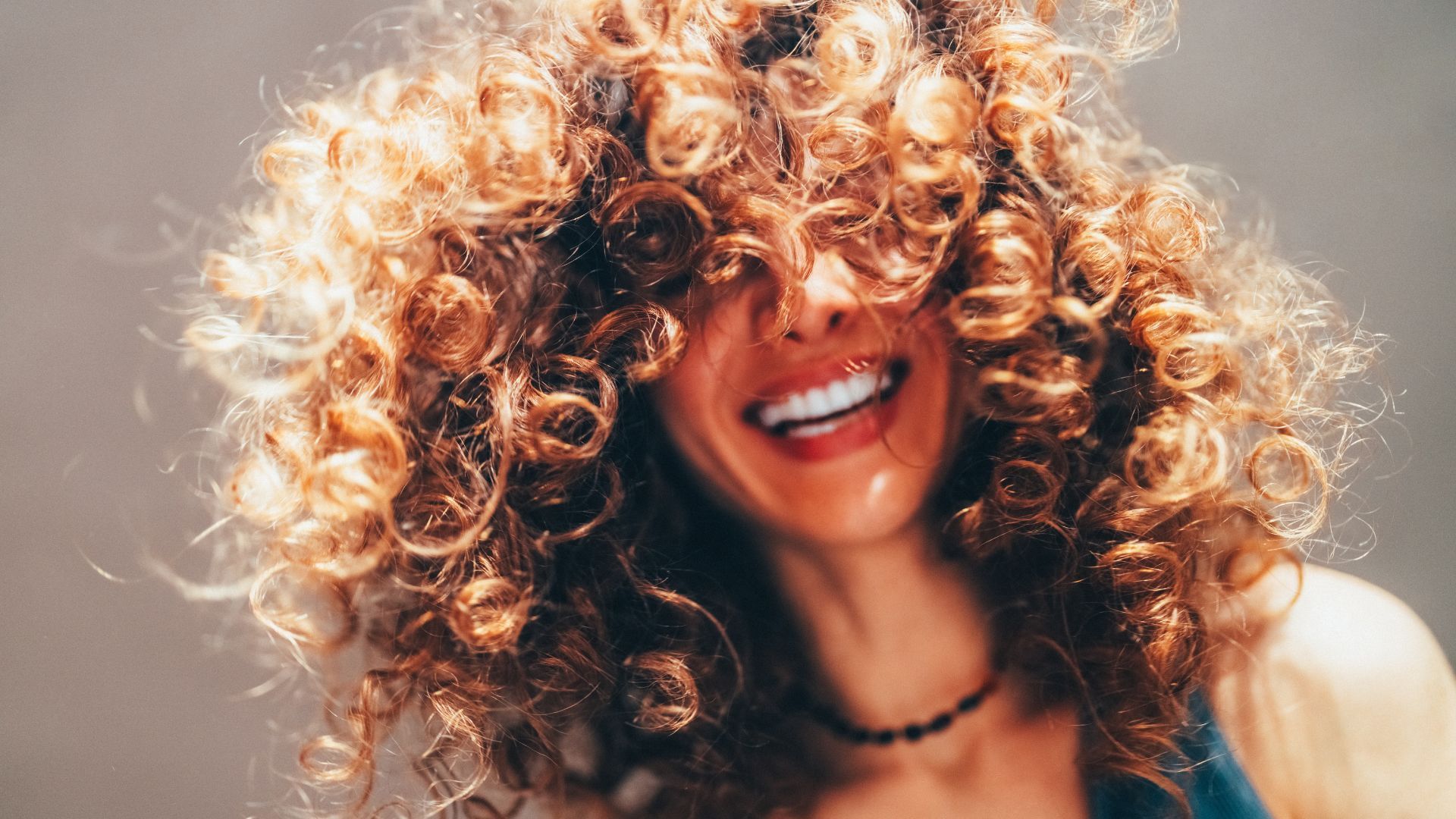 Lachende vrouw met krullend haar dat haar gezicht bedekt.